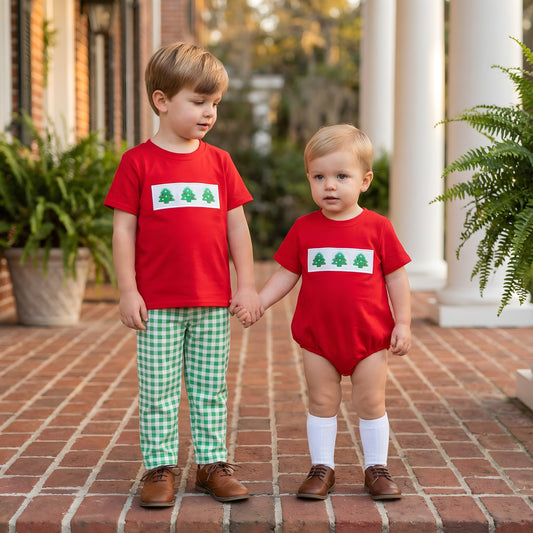 Two brothers holding hands on a brick porch wearing matching holiday outfits, featuring the Embroidered Christmas Tree Trio Boys Bubble on the toddler and a matching red shirt with green gingham pants on the older boy.