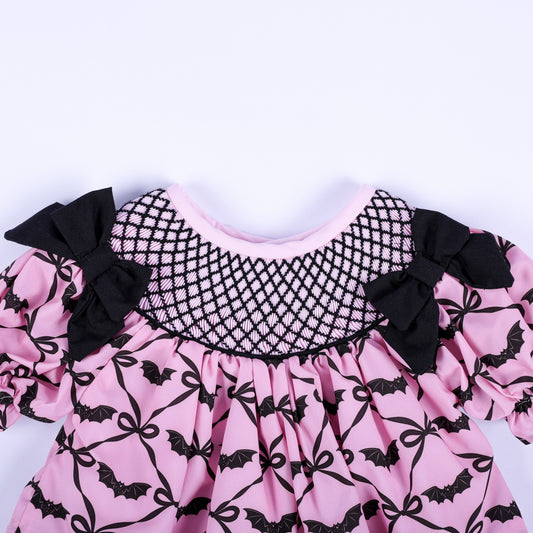 Hand smocked black lattice neckline detail on a pink bat pattern baby girl top with black side bows.