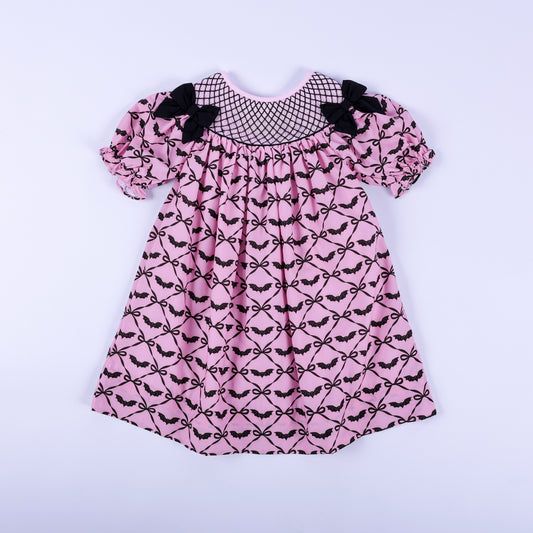 Pink hand smocked Halloween dress for girls featuring black bat bow print, black yoke embroidery, and puff sleeves.