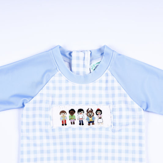 Close-up of boys hand smocked handsome prince rash guard chest featuring detailed hand embroidered fairytale figures.