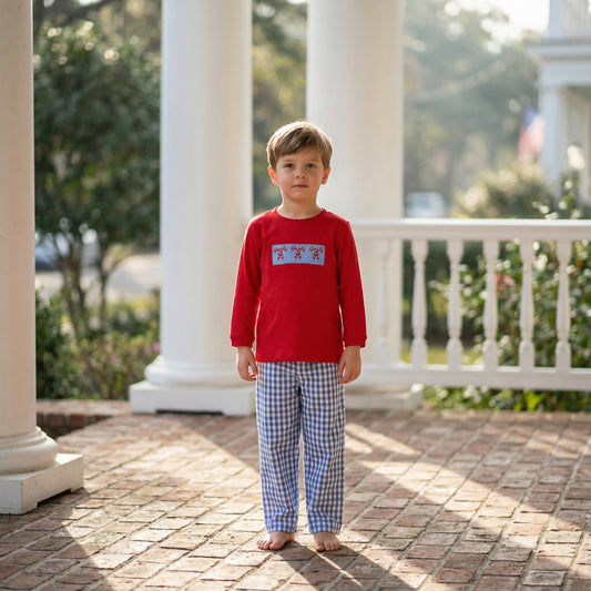 Boy in red hand smocked Christmas candy cane shirt and blue gingham pants set on porch.