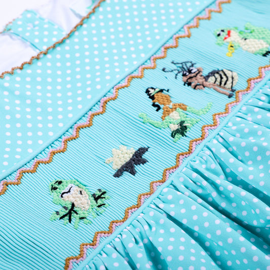 Detailed close-up of hand-smocked and hand-embroidered Frog Princess lotus design on aqua polka dot top.