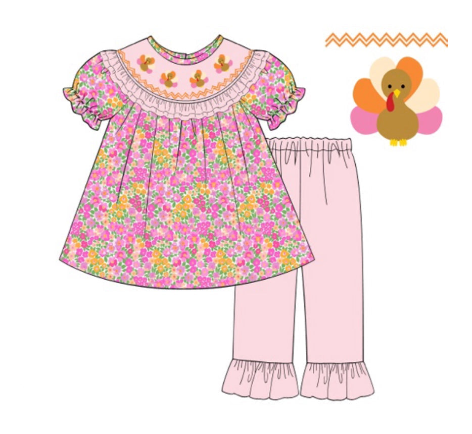 Two-piece girls Thanksgiving outfit featuring a pink and orange floral tunic top with smocked turkey details and matching light pink ruffle pants.
