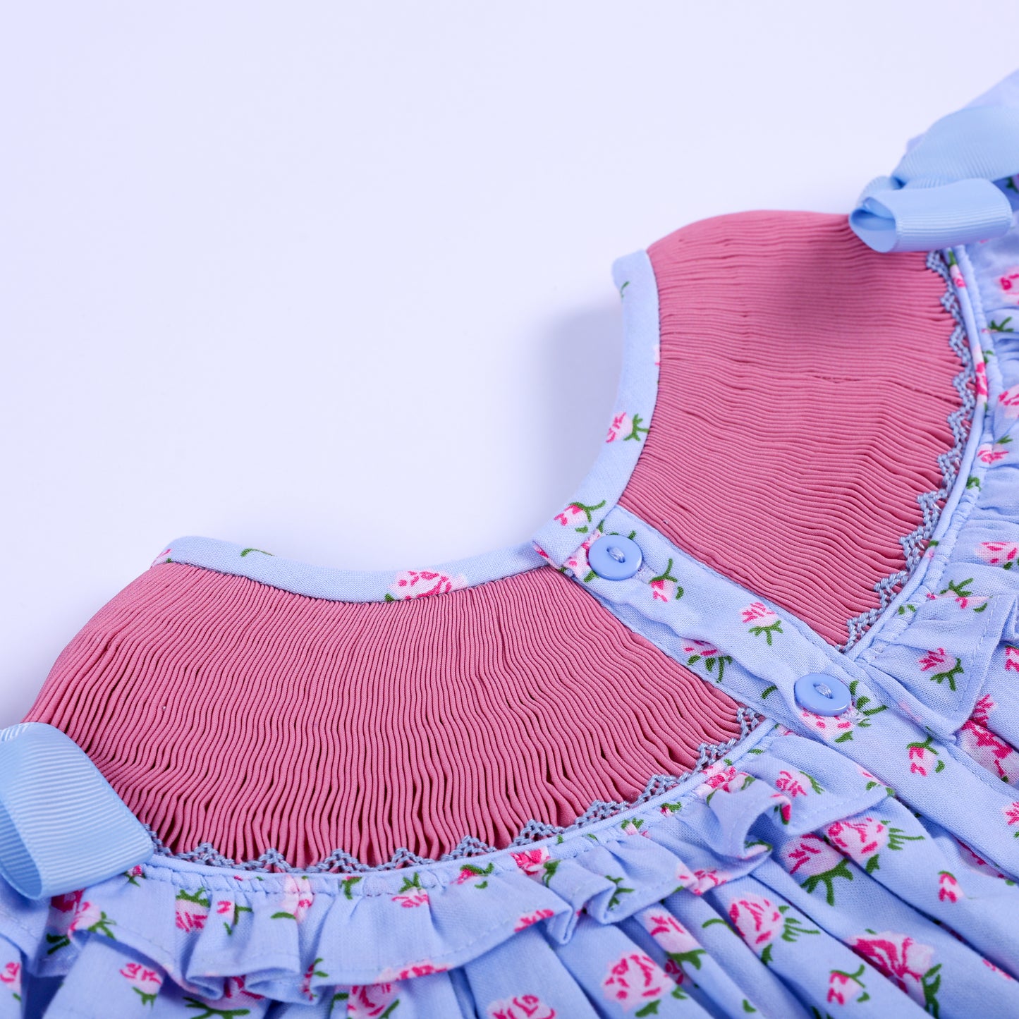 Close-up view of back button placket closure and pink smocked panel on girls floral hand-embroidered dress.