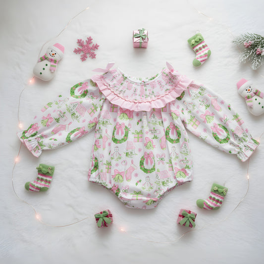 Flat lay of girls watercolor smocked Christmas bubble romper with pink garland print and festive holiday decor.