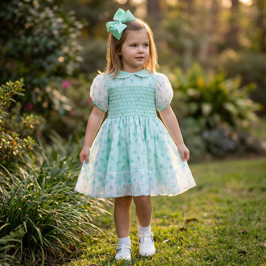 Little girl wearing the Hand Smocked Jenny’s Mint Chiffon Swiss Dot Rose Dress outdoors.