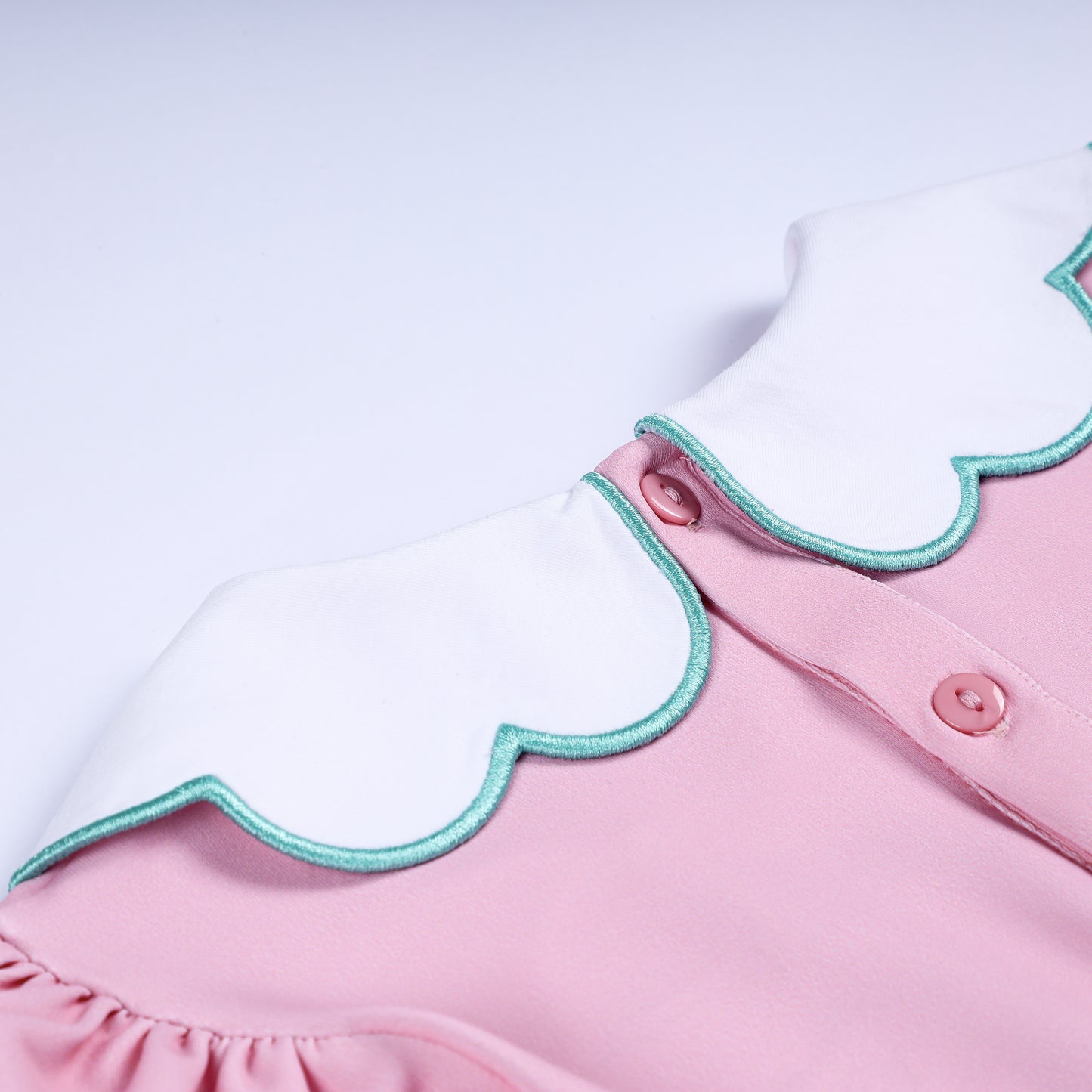 Back collar detail showing pink button closure on white scalloped Peter Pan collar with turquoise trim.
