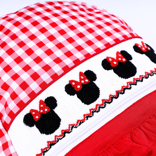 Close up of hand smocked mouse heads with red bows embroidered on a white band on red gingham backpack.