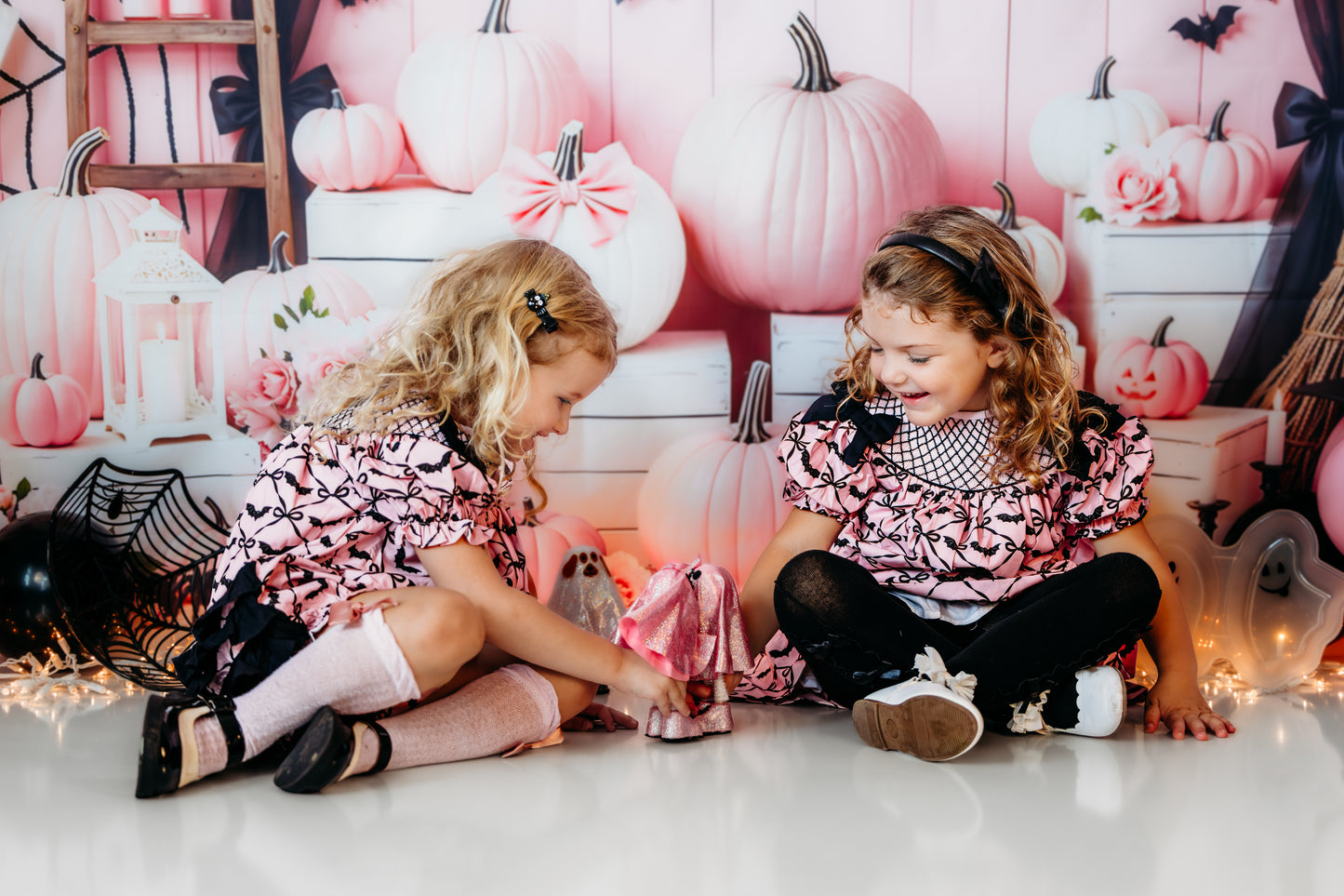 Two toddler girls playing in matching Batty for Bows hand smocked pink dresses with black embroidered bat pattern.