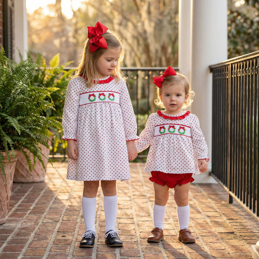 Matching siblings holding hands on a porch, wearing the Girls White Smocked Christmas Wreath Trio Dress and coordinating outfit.