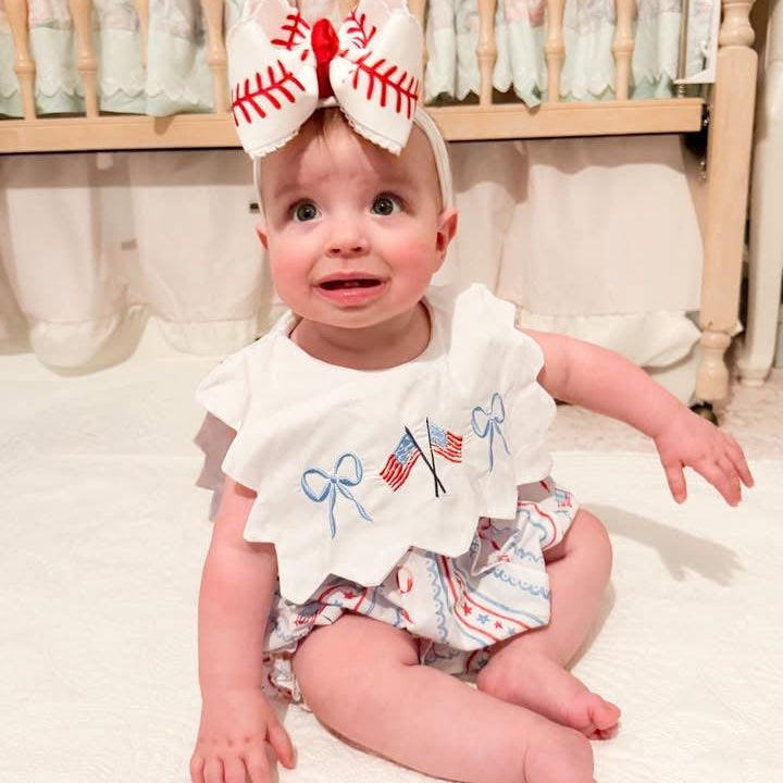 Baby girl sitting in Patriotic Grandmillennial embroidered bubble with scalloped collar and American flag bows.