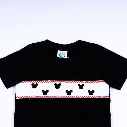 Close-up of hand smocked mouse silhouettes embroidered on white chest plate panel of black boys shirt.