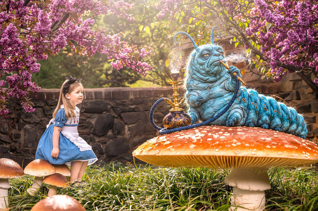 Little girl wearing an Alice-inspired blue smocked dress and white pinafore by Smocked Peacock, seated in a whimsical fairytale garden across from the Blue Caterpillar.   
