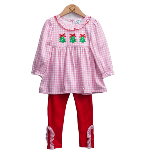A girls' two-piece holiday outfit set displayed on a wooden hanger. The top is a long-sleeved pink and white gingham tunic featuring a ruffled collar with red trim and three green Christmas tree appliqués with red bows across the chest. The matching bottoms are solid bright red leggings finished with pink and white gingham ruffles at the ankles.