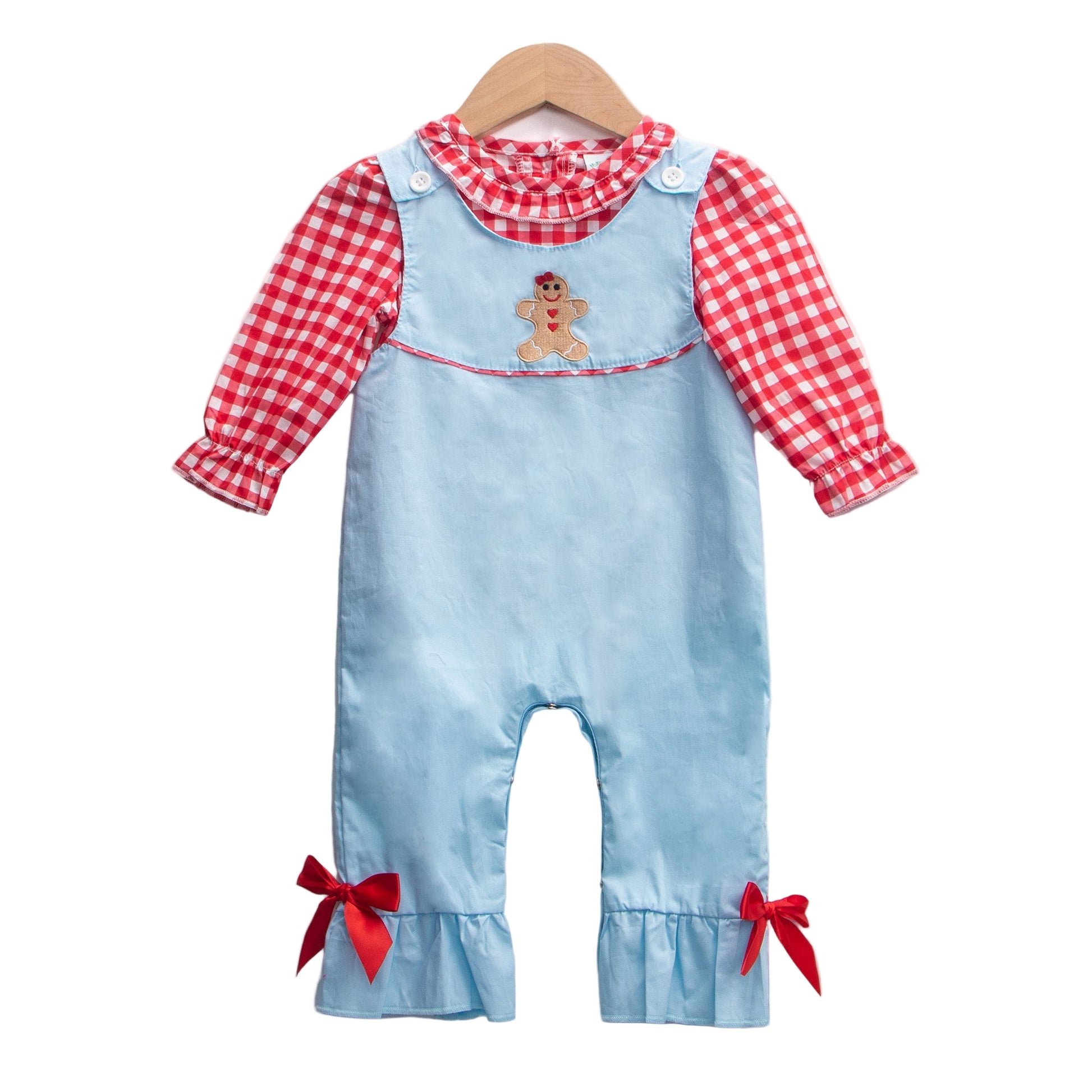 Baby girl Christmas outfit set featuring a light blue romper with a gingerbread man applique on the chest and red bows at the ruffled ankles, layered over a red and white gingham check long-sleeved shirt with a ruffled collar, hanging on a wooden hanger against a white background.