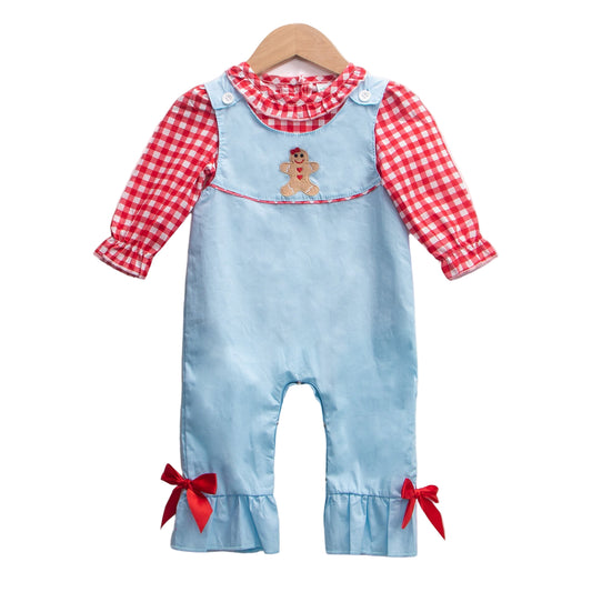 Baby girl Christmas outfit set featuring a light blue romper with a gingerbread man applique on the chest and red bows at the ruffled ankles, layered over a red and white gingham check long-sleeved shirt with a ruffled collar, hanging on a wooden hanger against a white background.