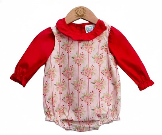 A baby romper displayed on a wooden hanger. The romper has long red sleeves and a ruffled neckline, with a white front featuring a repeating pattern of pink bows and green leaves. The bottom is gathered with elastic leg openings.