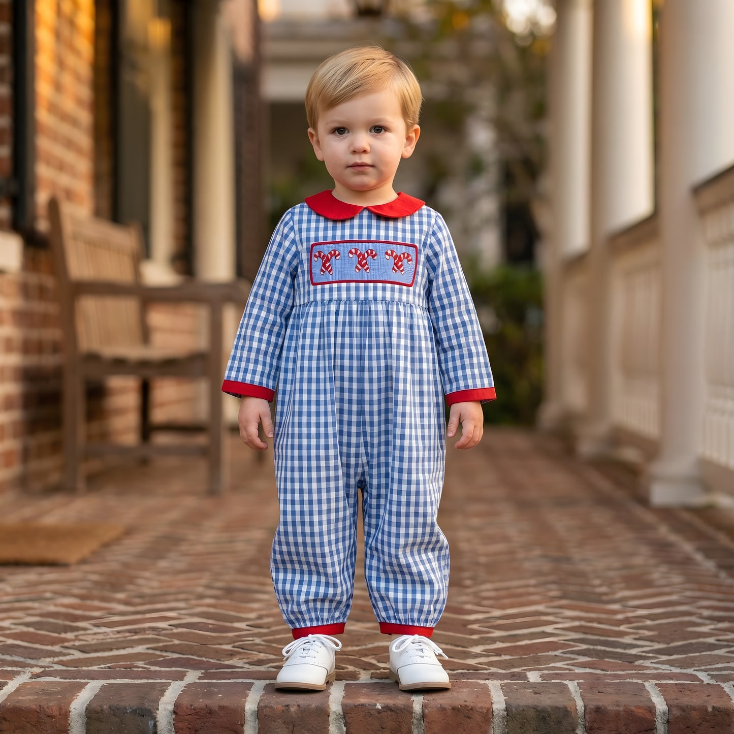 Toddler wearing a blue gingham Boys Hand Smocked Christmas Candy Cane Romper with red collar and cuffs.