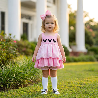 Toddler girl standing outdoors wearing a Pink Bow Mouse French Knot Bloomer Set featuring a tiered gingham design, lace trim, and saddle shoes.
