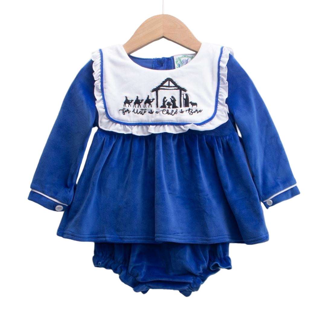 A baby diaper set displayed on a wooden hanger. The set includes a long-sleeve royal blue top with white trim on the cuffs and a white bib-style collar featuring an embroidered nativity scene and the phrase ‘For Unto Us a Child is Born.’ Matching royal blue diaper cover is visible underneath