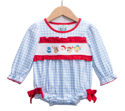 A blue and white gingham baby romper on a wooden hanger, featuring a white smocked panel with red ruffles and embroidered Christmas characters including Santa, reindeer, an elf, and a blue monster. The long-sleeved outfit has red ruffle trim at the cuffs and red bows on the leg openings.
