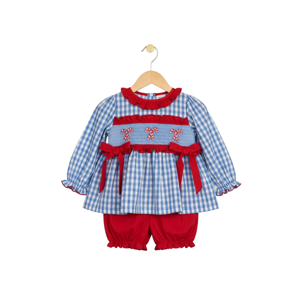 A two-piece baby girl's outfit on a wooden hanger, featuring a blue and white gingham long-sleeved top with red ruffled trim, a smocked panel with embroidered candy canes and red bows, and matching solid red bloomers.