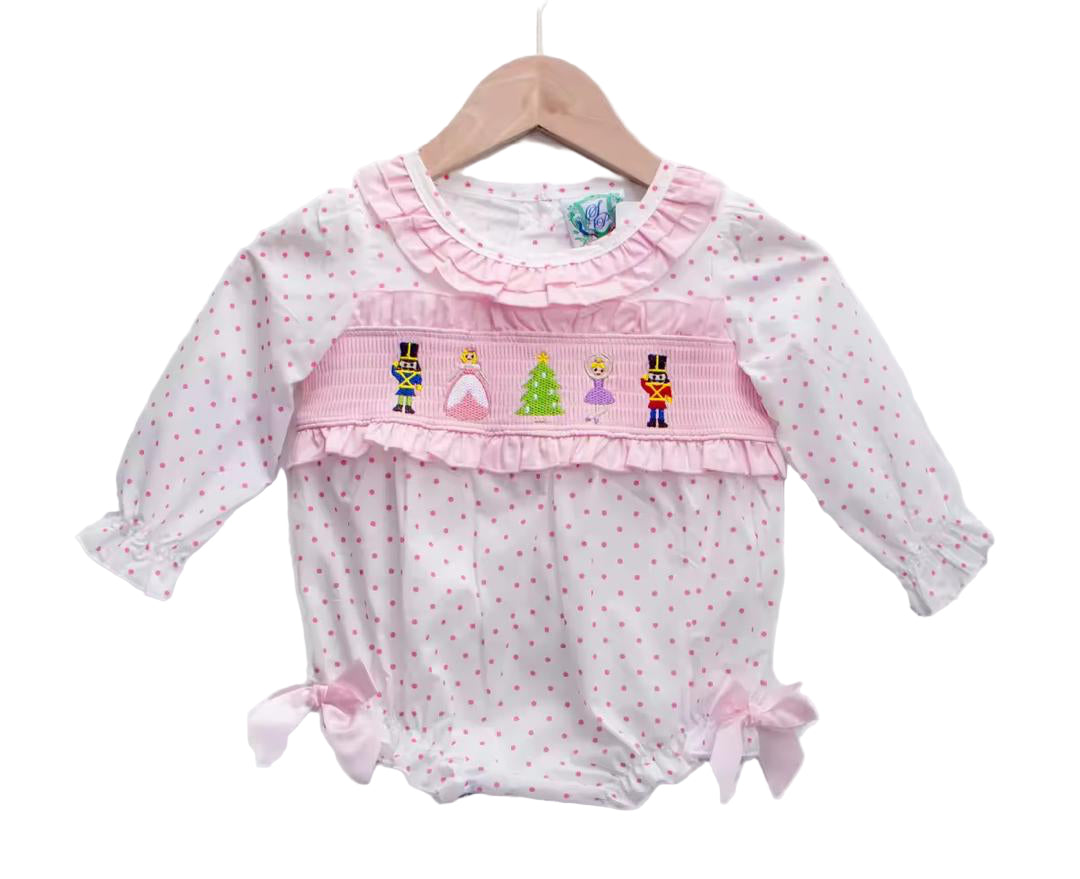 Baby girls pink smocked bubble romper featuring embroidered Nutcracker, Clara, and Christmas tree details on white and pink polka dot fabric with satin side bows and ruffled collar.