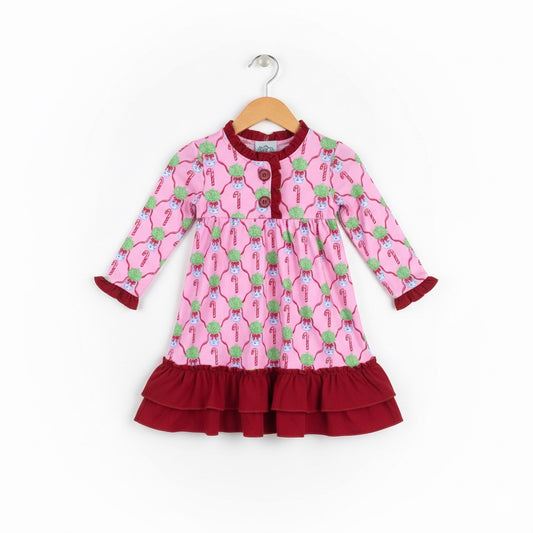 A pink long-sleeved girls' nightgown hanging on a wooden hanger. The nightgown features a festive repeating pattern of candy canes and blue ornaments topped with green foliage. It is accented with deep burgundy ruffles at the neckline, button placket, and sleeve cuffs, and finishes with a wide, double-tiered burgundy ruffle at the bottom hem.