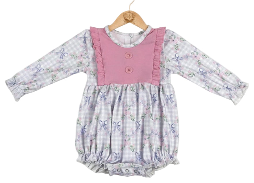 Grandmillennial floral girls bow bubble romper featuring a lavender gingham print with pink roses and blue bows, accented by a solid pink ruffled bib with buttons and long sleeves.