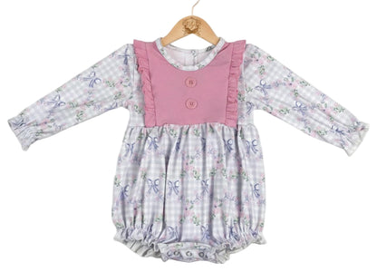 Grandmillennial floral girls bow bubble romper featuring a lavender gingham print with pink roses and blue bows, accented by a solid pink ruffled bib with buttons and long sleeves.