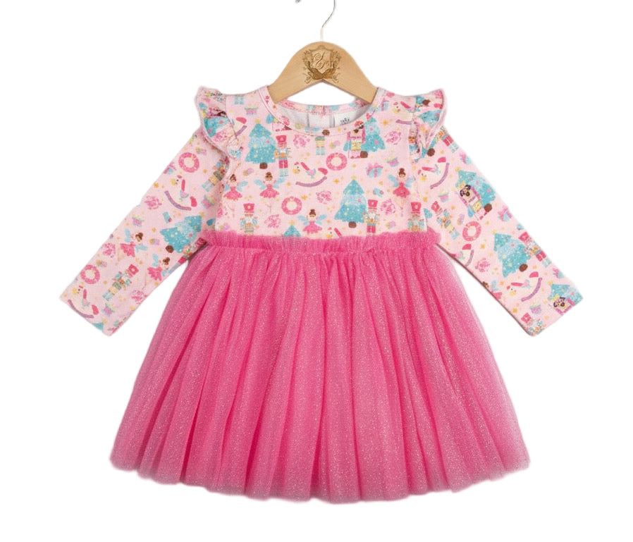 A girl's pink long-sleeve Christmas tutu dress with a nutcracker and angel print bodice and a bright pink tulle skirt, hanging on a wooden hanger against a white background.
