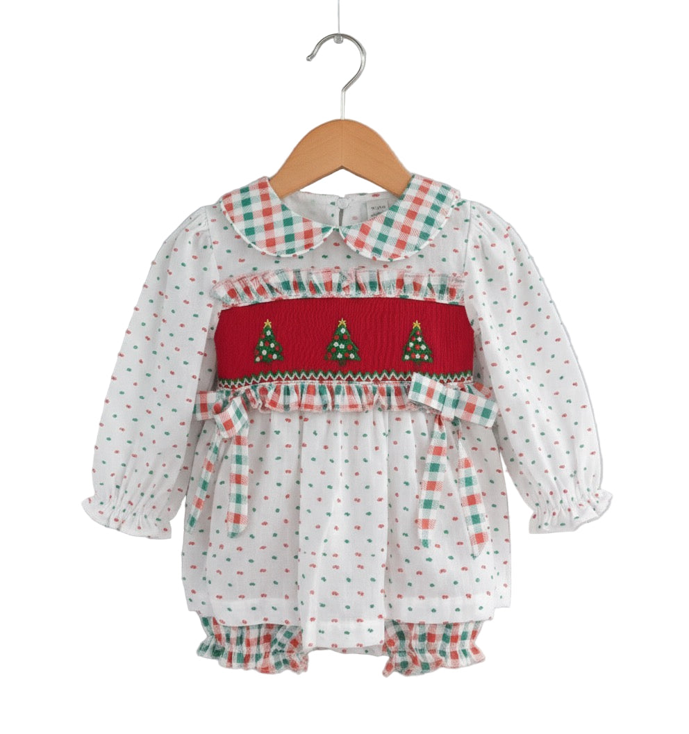A white baby dress and matching bloomer set on a wooden hanger, featuring small red and green dots, a red smocked bodice with three embroidered Christmas trees, and a red and green gingham peter pan collar, sleeve cuffs, waist bows, and bloomer ruffle.