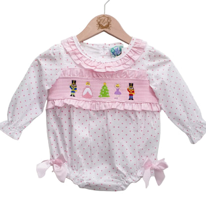 Baby girls pink smocked bubble romper featuring embroidered Nutcracker, Clara, and Christmas tree details on white and pink polka dot fabric with satin side bows and ruffled collar.