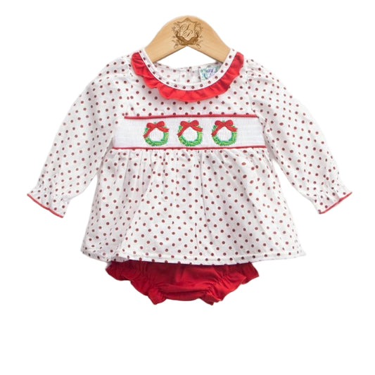 A baby diaper set displayed on a wooden hanger. The set includes a long-sleeve white top with red polka dots, a ruffled red neckline, and a smocked chest panel embroidered with three green wreaths tied with red bows. Matching red diaper cover is visible underneath.