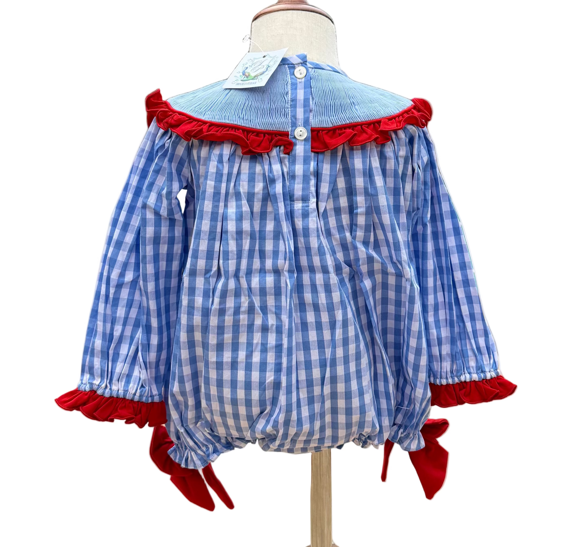 Back view of a child's blue and white gingham bubble romper displayed on a mannequin. The garment features a light blue smocked yoke trimmed with a vibrant red ruffle, long sleeves with matching red ruffled cuffs, and red bows at the leg openings. A button-down placket runs down the center of the back.