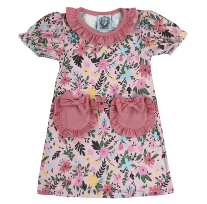 Field Of Flowers Spring Pocket Dress featuring a pink floral print, ruffled neckline, puff sleeves, and two front pockets accented with bows.