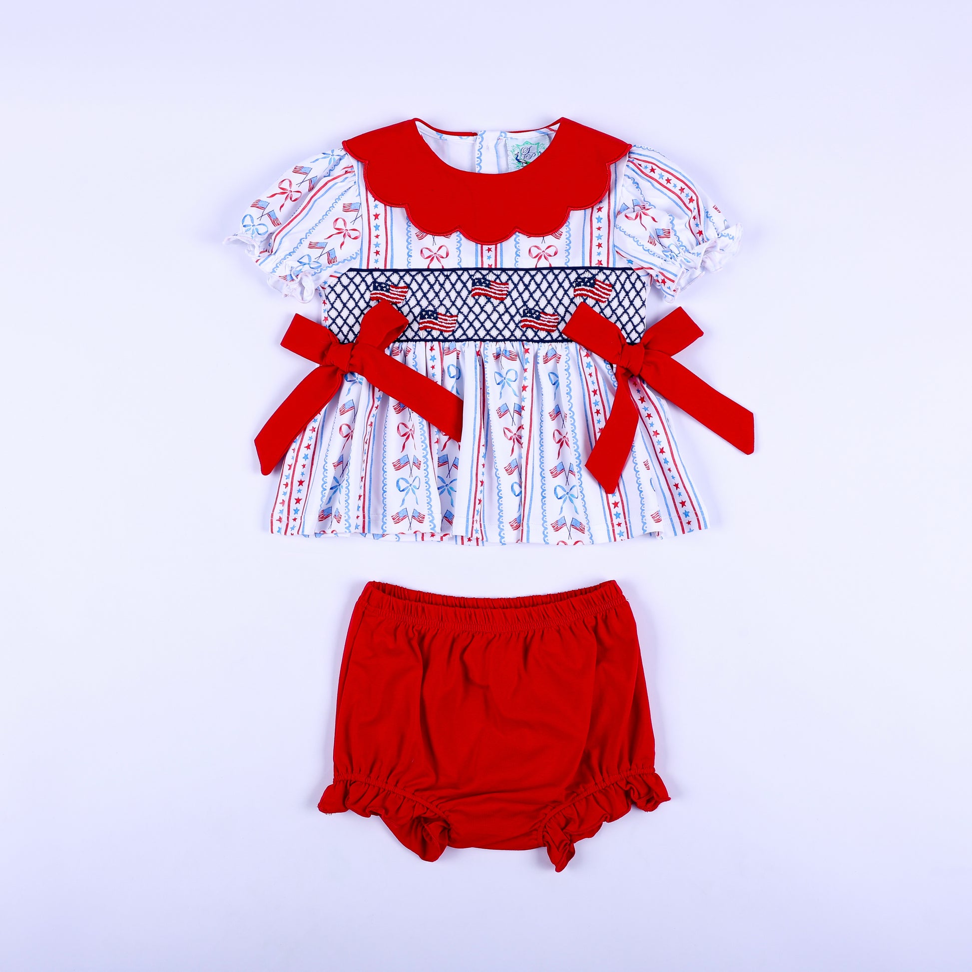 Full front view of America the Beautiful hand smocked baby girl bloomer diaper set featuring embroidered US flags.