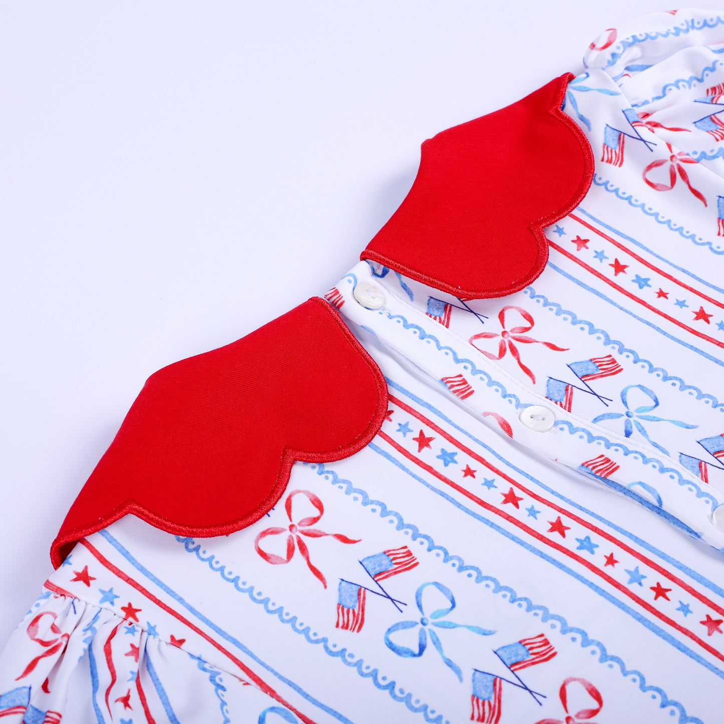 Detailed view of red scalloped collar and pearl button closure on back of girls hand embroidered patriotic dress.