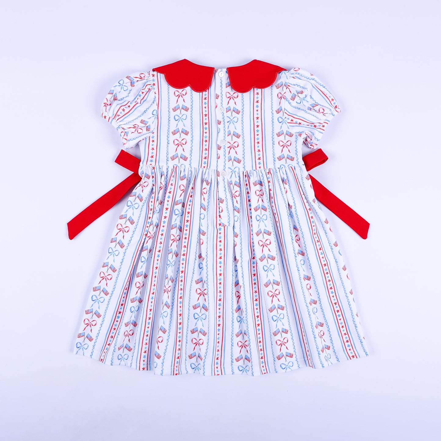 Full back view of America the Beautiful hand smocked dress showing button closure and tied red side sashes.