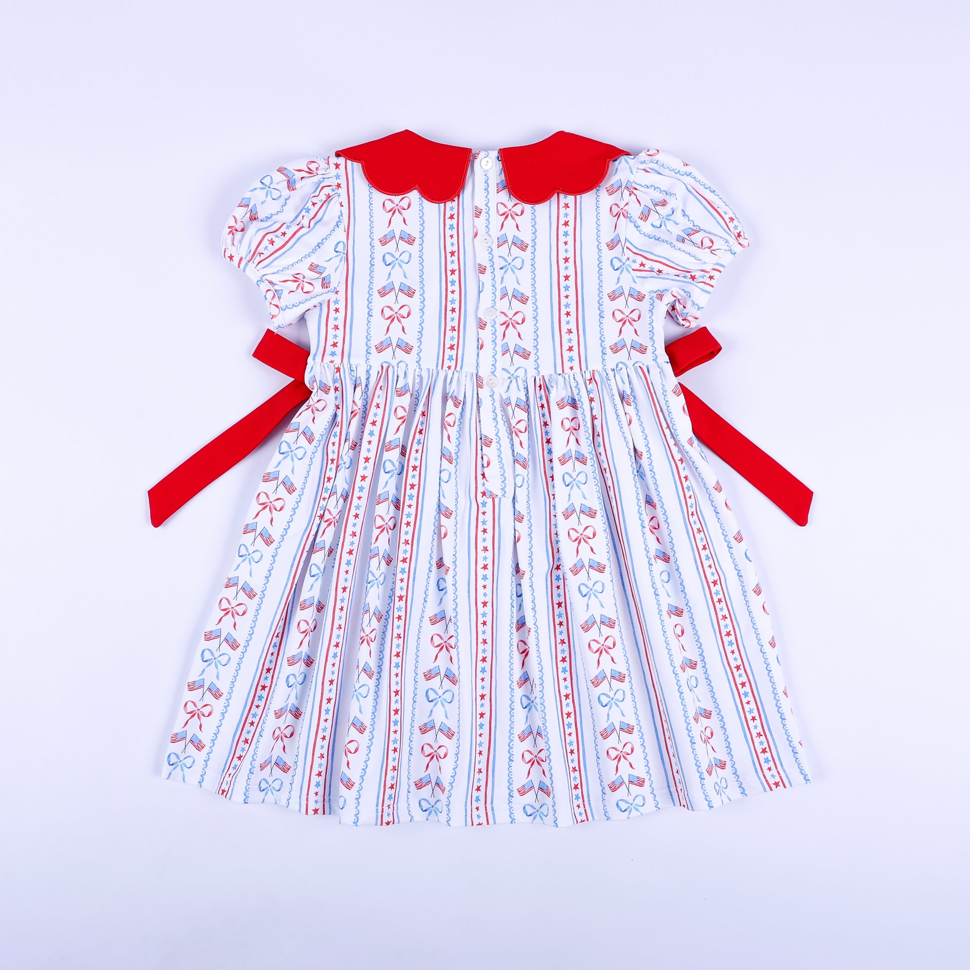 Full back view of America the Beautiful hand smocked dress showing button closure and tied red side sashes.