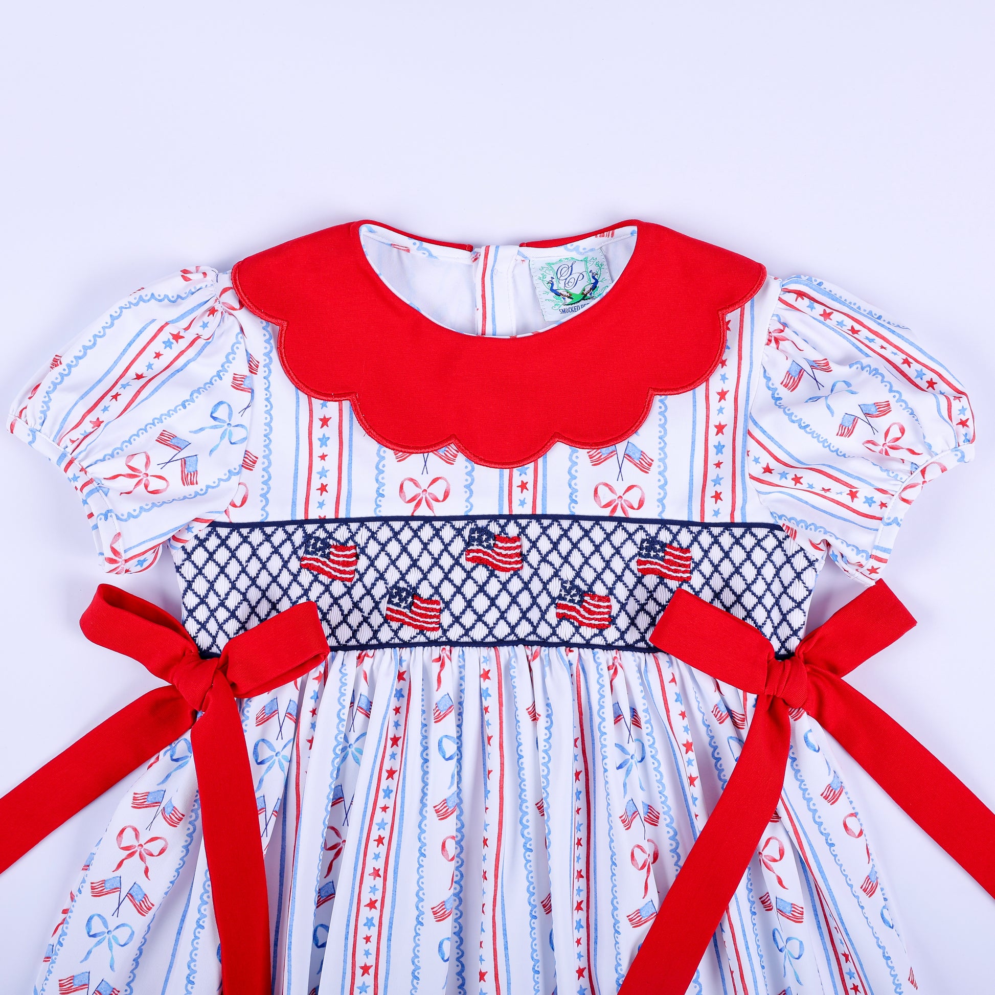 Close-up view of hand smocked American flags on the bodice of the girls red white and blue patriotic party dress.