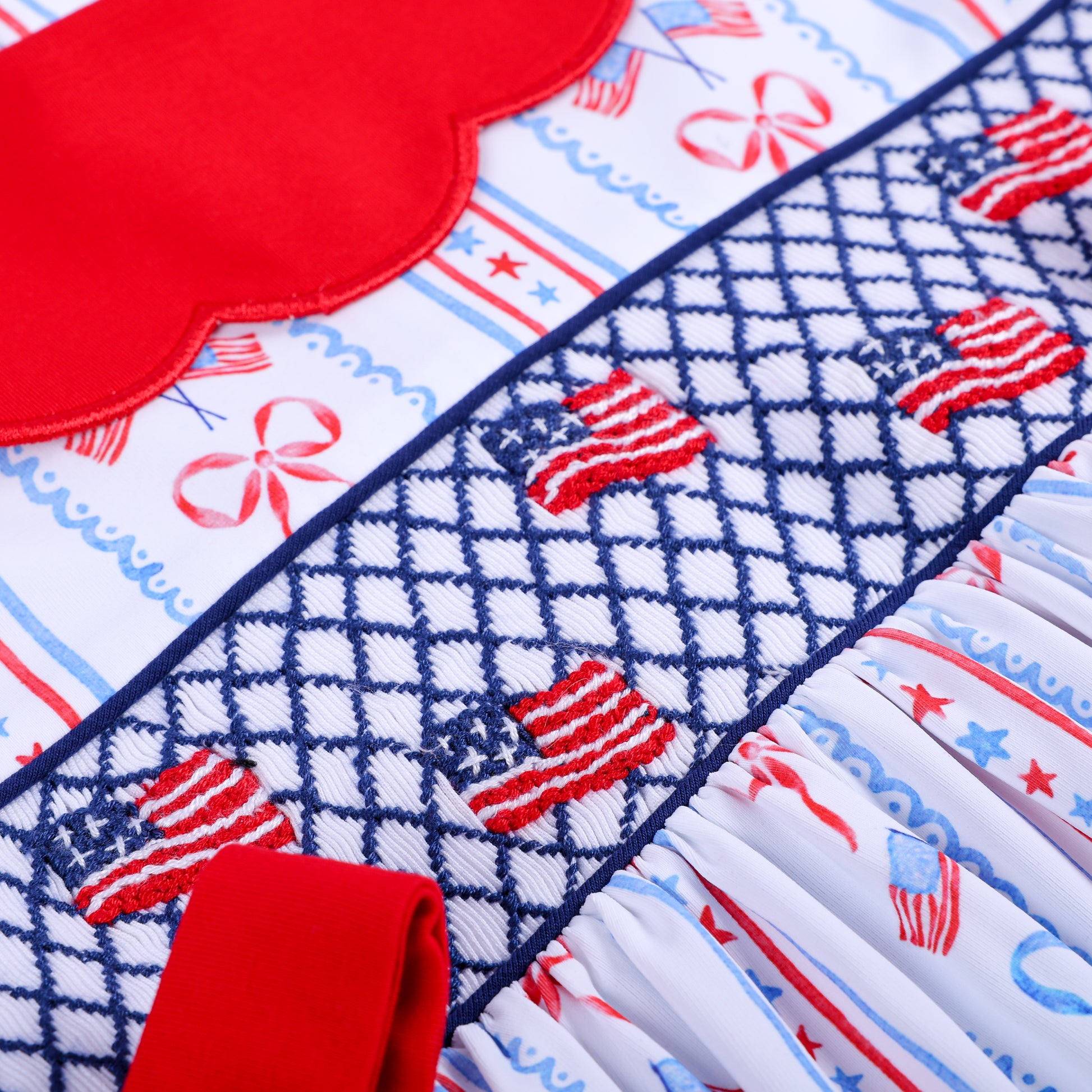 Detailed close-up of intricate navy smocking and hand embroidered red and white American flags on girls dress.