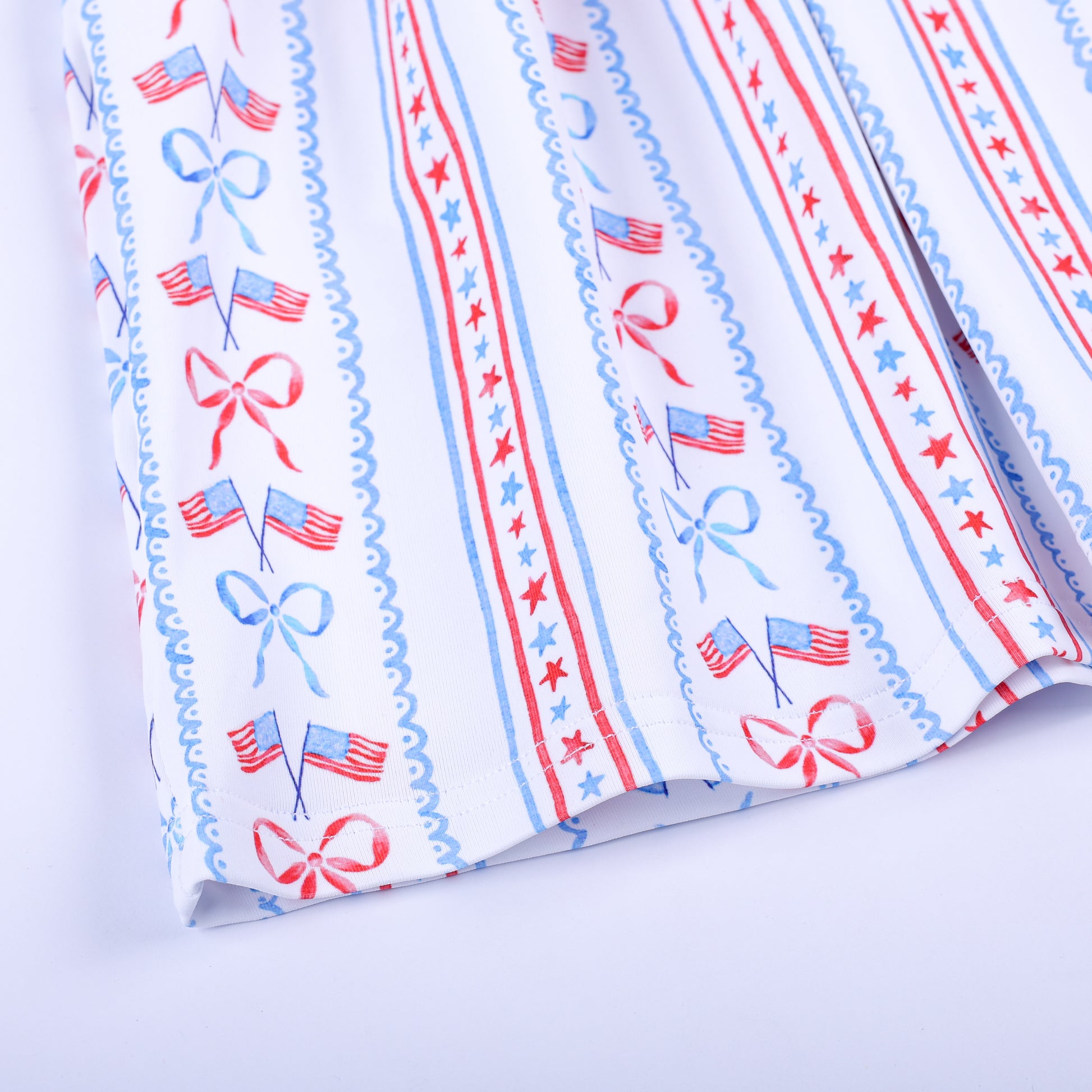 Close-up of patriotic print fabric featuring American flags, red bows, and stars on the skirt hem of girls dress.