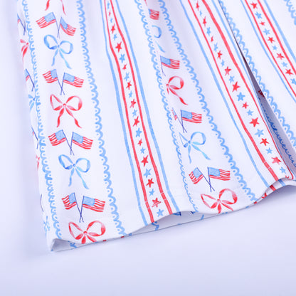Close-up of patriotic print fabric featuring American flags, red bows, and stars on the skirt hem of girls dress.