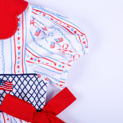 Detailed view of puff sleeves, red side bow tie, and hand embroidered American flag details on girls smocked dress.