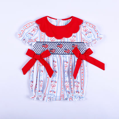 Front view of America the Beautiful hand smocked baby bubble with a red scalloped collar and embroidered US flags.