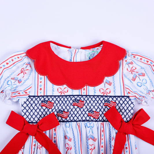 Close-up of hand-smocked bodice with embroidered American flags and red bows on patriotic baby outfit for 4th of July.