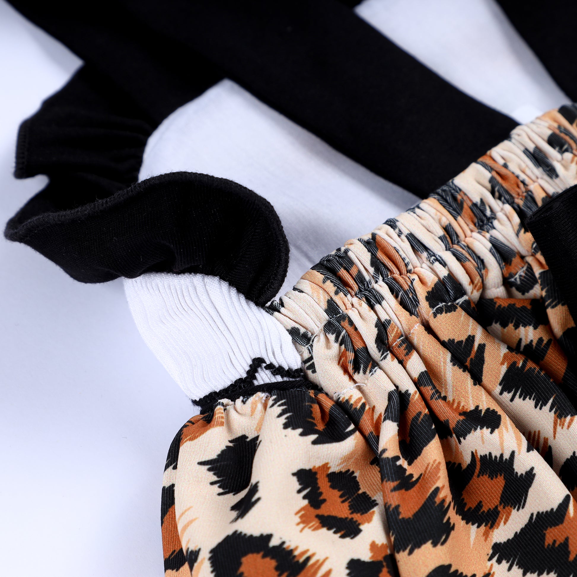 Close-up back detail of animal kingdom leopard print straps, ruffle trim, and back bow elastic on smocked baby top.