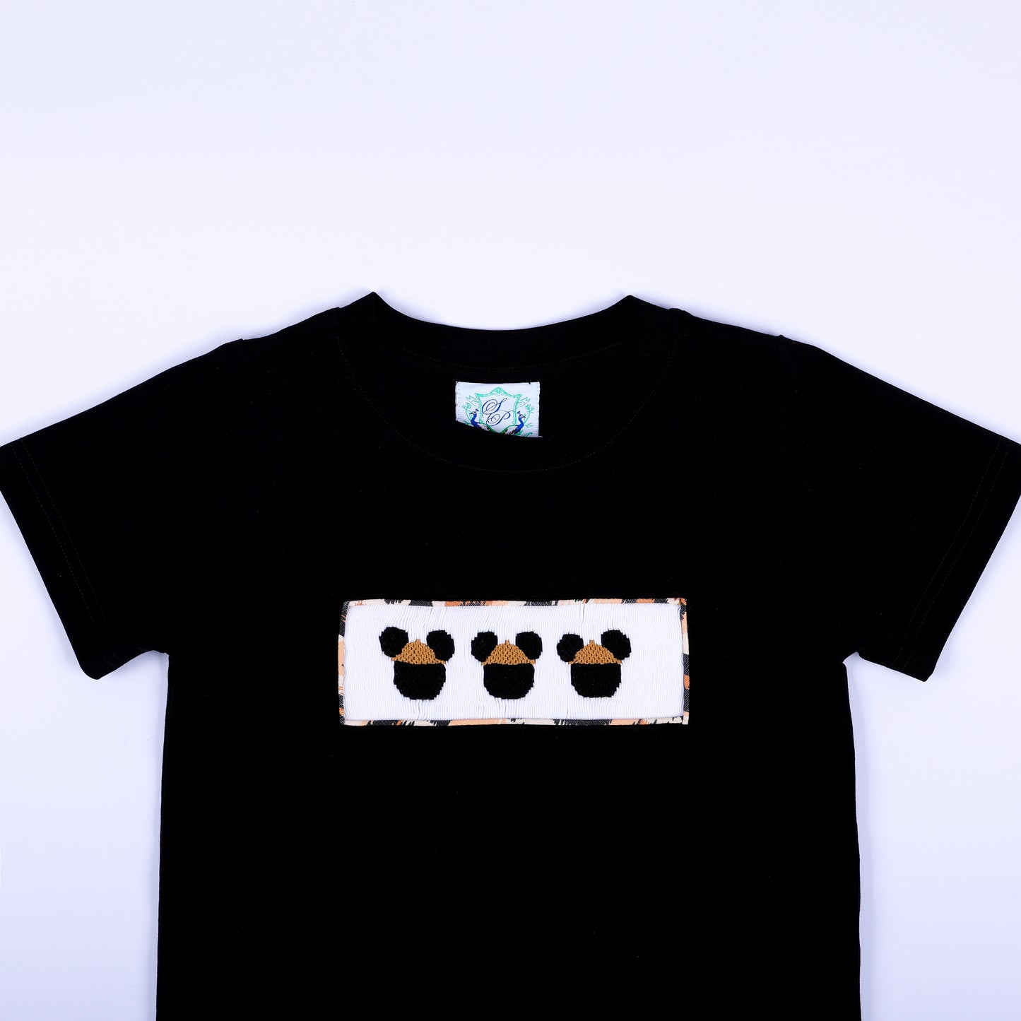 Close-up of boys black crewneck t-shirt featuring hand smocked safari mouse embroidery plate on chest.