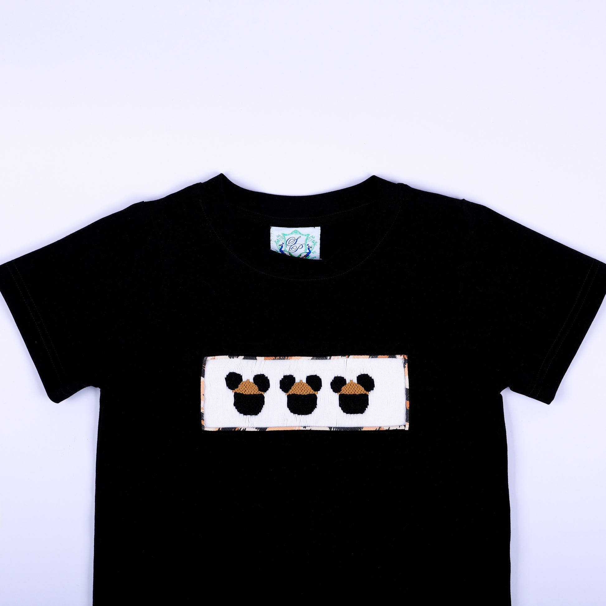 Close-up of boys black crewneck t-shirt featuring hand smocked safari mouse embroidery plate on chest.